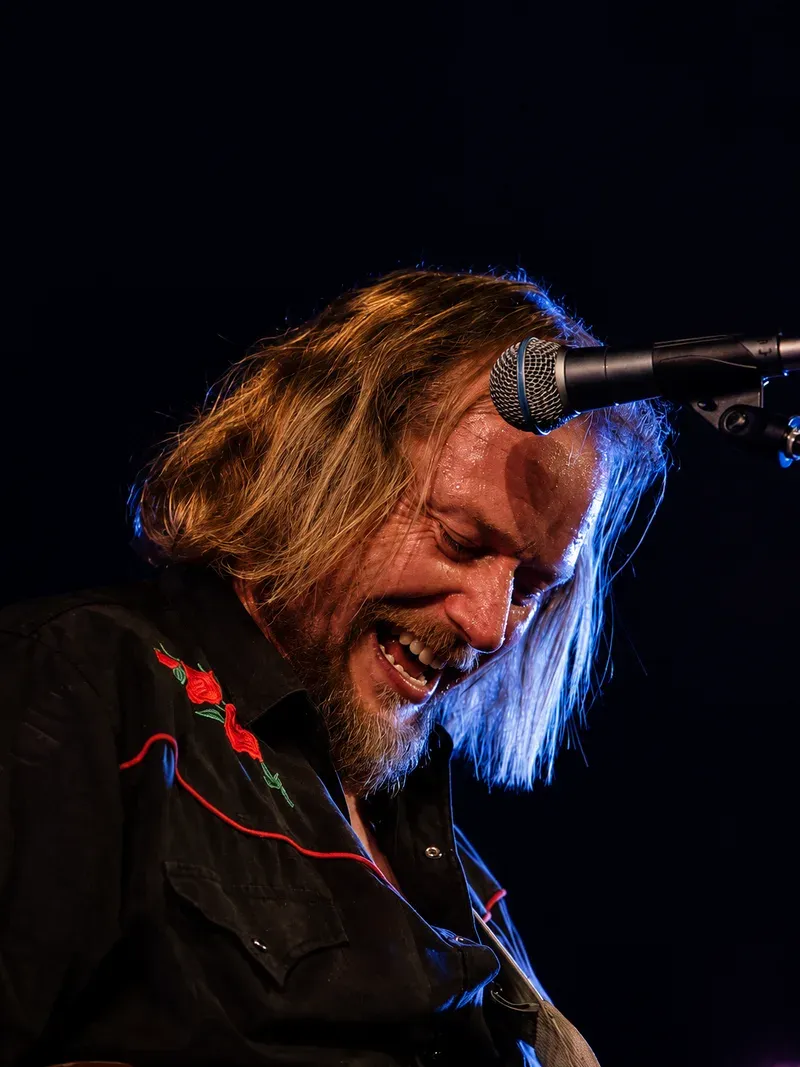 Mats Nerli med langt hår, syngende inn i mikrofonen med gitaren