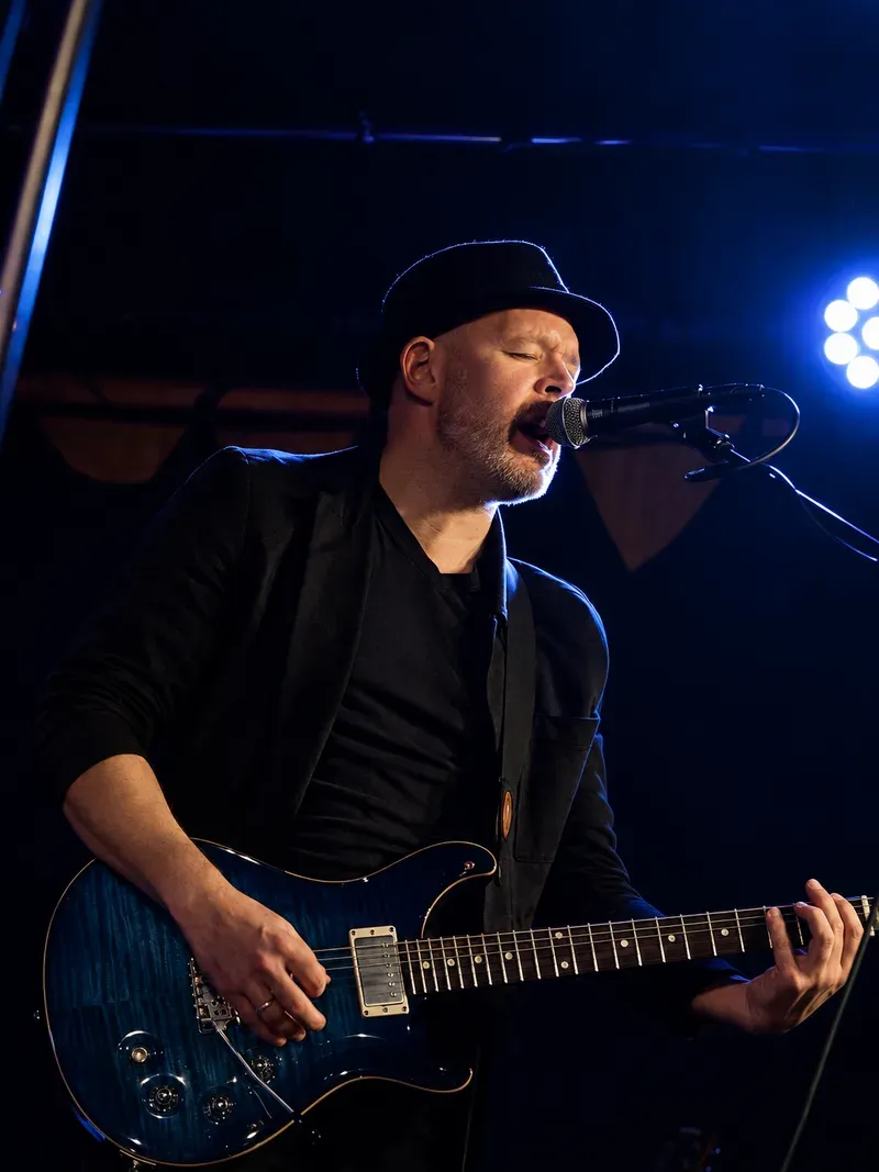 Terje Ræstad med hatt, syngende inn i mikrofonen med den blå gitaren